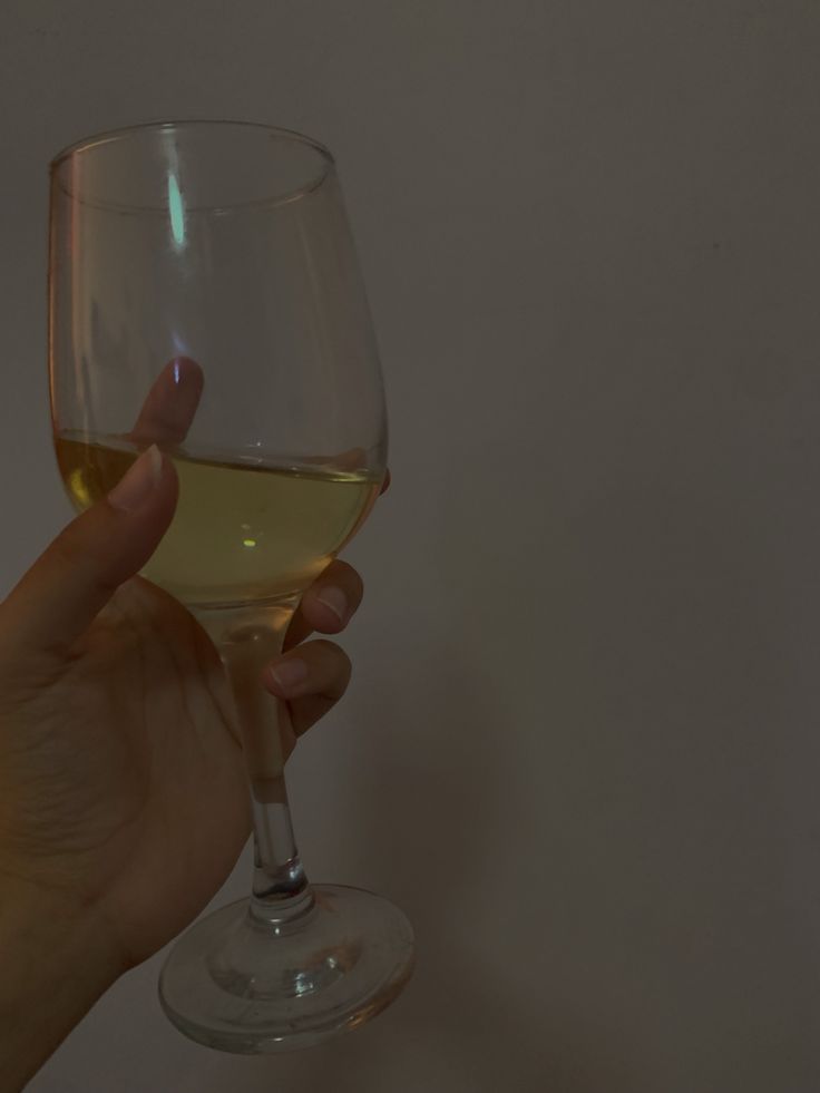 a person holding a wine glass with white wine in it's hand, against a plain background