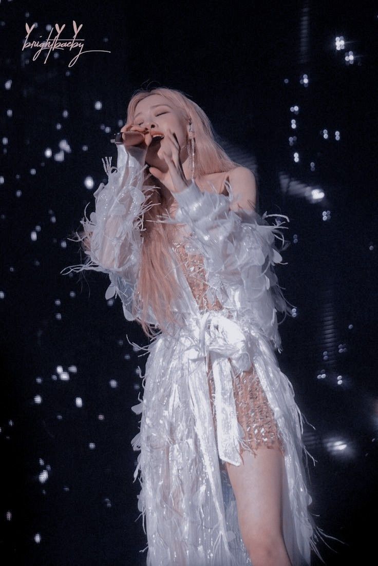 the woman is dressed in white feathers and holding her hand up to her face as she sings