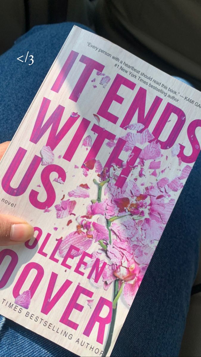 a person is holding up a book in their lap, with the title it ends with us written on it