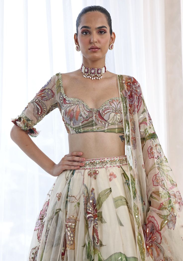 Featuring an ethereal ivory lehenga in a summer print and adorned with delicate embroidery. Paired perfectly with a matching classic blouse with a ruffle detail and a printed dupatta with glam sequins. This floral lehenga radiates elegance and grace and is ideal for a Sangeet or Mehendi at a destination party ! Composition : Lehenga, Blouse, Dupatta - Organza Care: Dry Clean Only and Vacuum Storage This product can be customized for sleeves, length of blouse and neckline Delivery : 4-6 weeks as the product is hand crafted. Check Size Guide or choose MySize for free customisation (All Sizes above XL can be made at 15% additional cost) For more information and sizes please contact fabiliciousfashion@gmail.com or visit our Copenhagen studio. About the Designer : Mahima Mahajan is best known f Designer Floral Print Organza Choli, Floral Print Organza Sharara For Navratri, Floral Organza Sharara For Navratri, Floral Print Organza Lehenga With Traditional Drape, Elegant Floral Print Georgette Sharara, Navratri Floral Print Organza Lehenga, Elegant Silk Anarkali Set With Floral Print, Organza Sharara With Floral Print In Traditional Drape, White Anarkali Lehenga With Floral Print