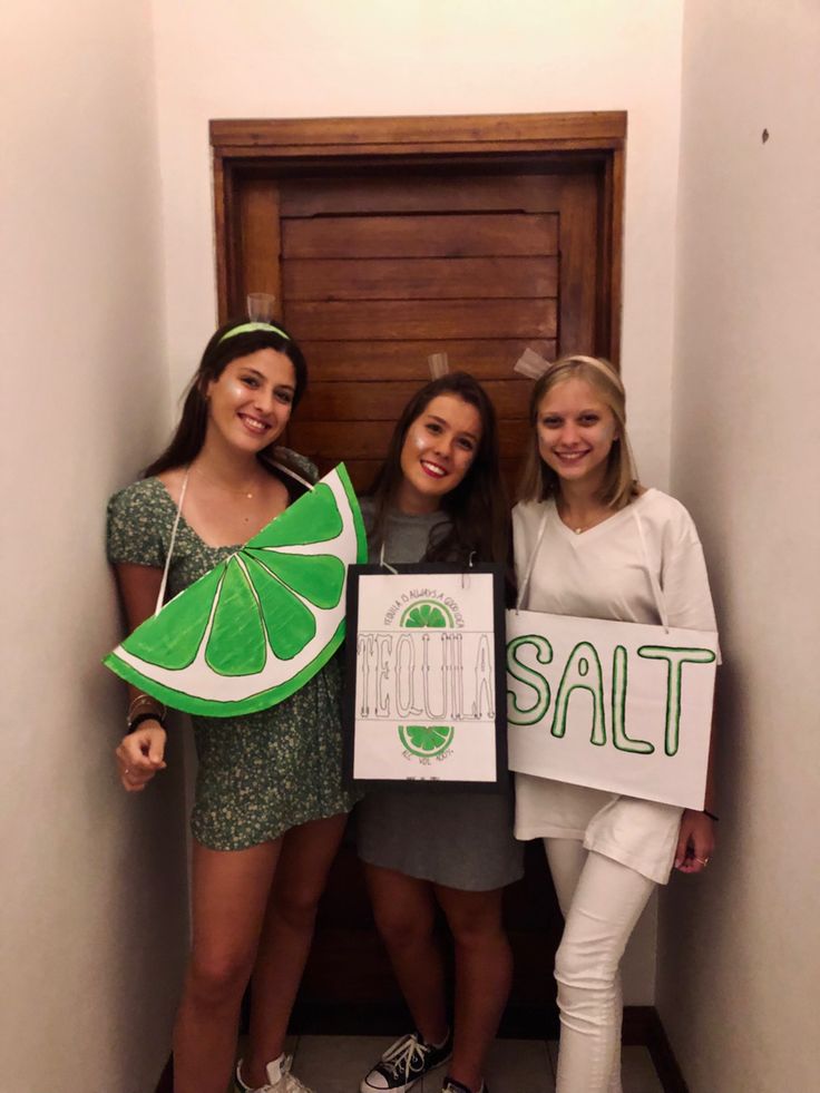 three girls are holding signs and smiling for the camera while standing in front of a door