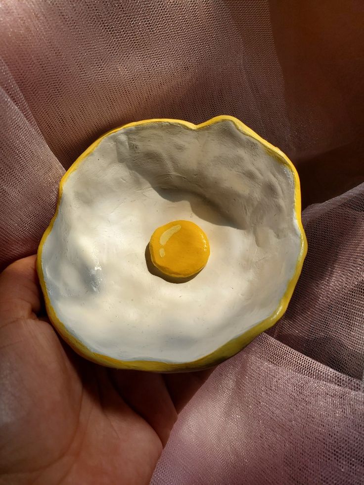 a hand holding a yellow and white bowl with an egg in it's center