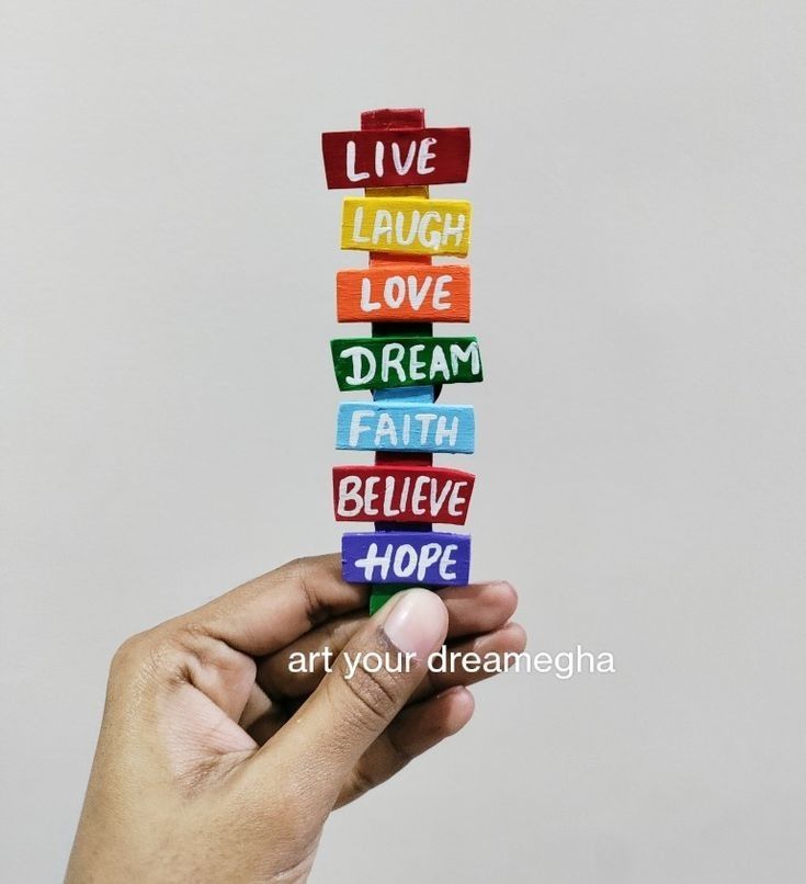 a hand holding a stack of colorful blocks with words written on them that say live laugh love dream faith believe hope