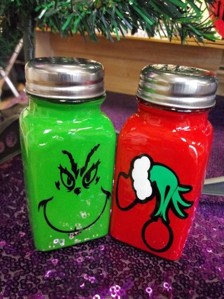 two jars with faces painted on them sitting next to each other in front of a christmas tree