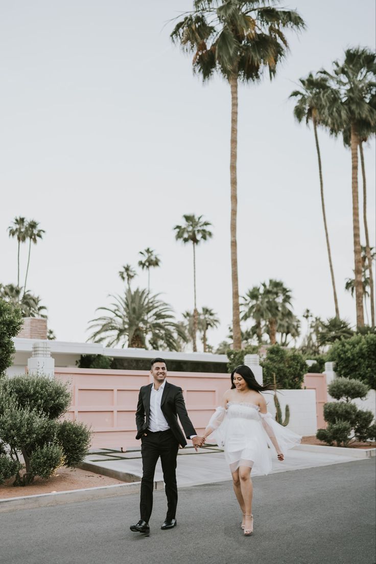 a newly married couple holding hands and walking down the street in front of palm trees