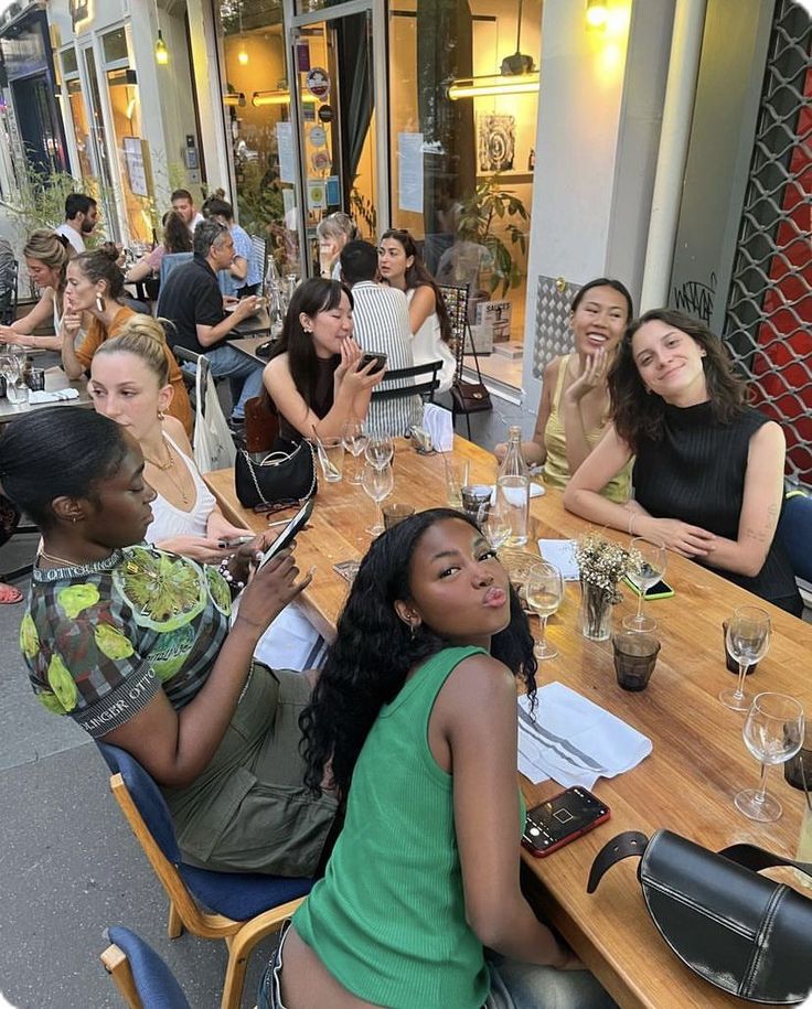 a group of people sitting around a wooden table with wine glasses on top of it