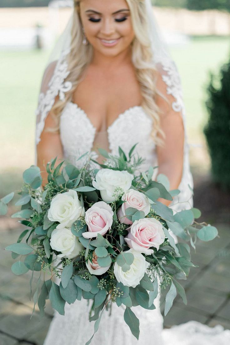 a bride holding a bouquet of flowers and greenery in her hands while smiling at the camera