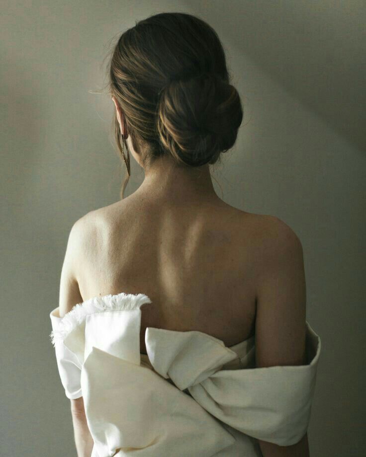 a woman in a white dress with her back to the camera, wrapped in a blanket