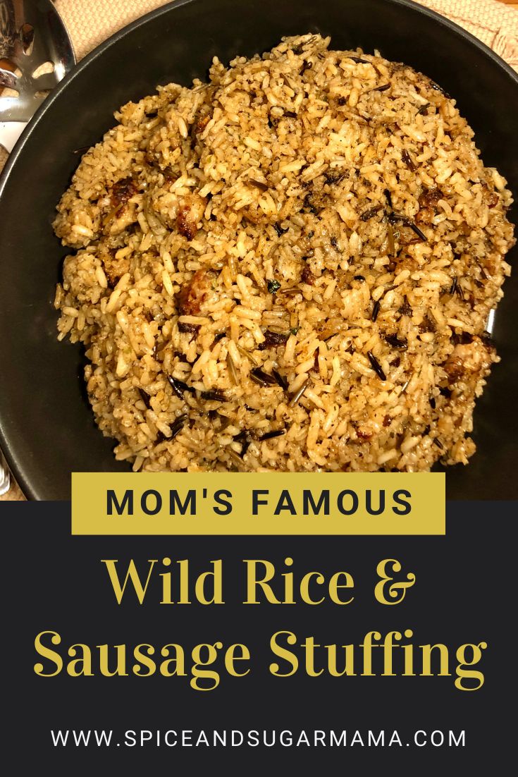 wild rice and sausage stuffing in a black bowl on a table with spoons, fork and utensils