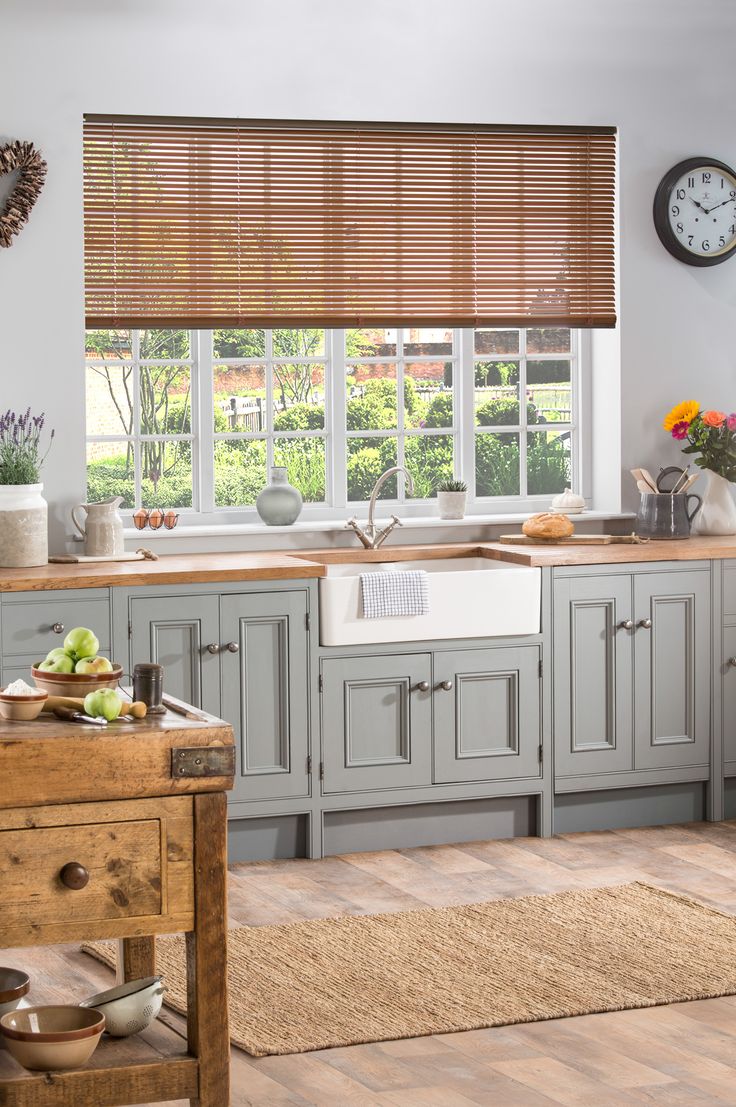 a kitchen with gray cabinets and wooden blinds on the window sill above the sink