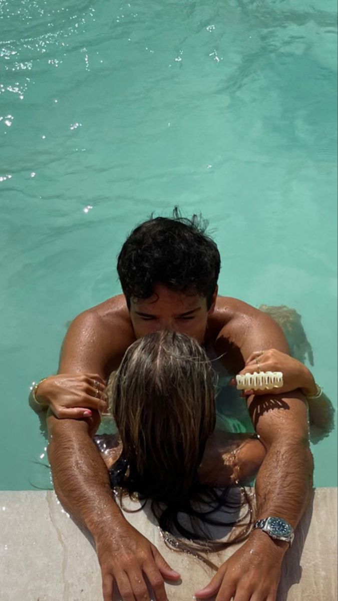 a man and woman sitting in the middle of a pool with their arms around each other