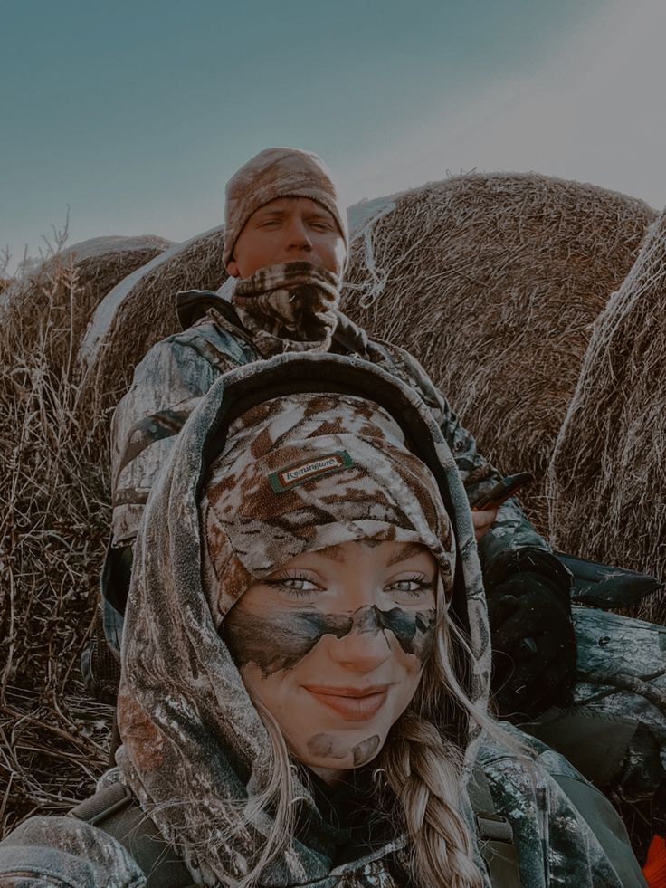 a man and woman with camouflage paint on their faces standing in front of hay bales