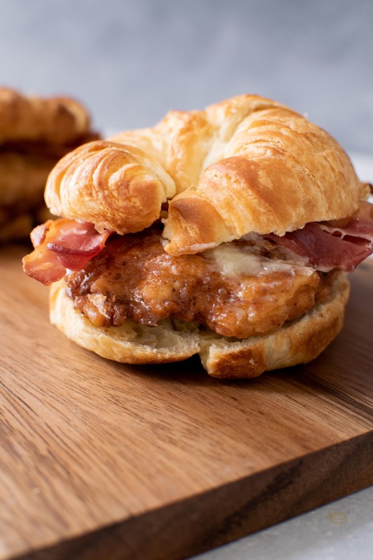 a croissant sandwich with meat and cheese on a wooden cutting board next to some pretzels