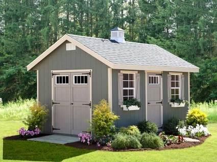 a small gray shed with windows and flowers in the front yard