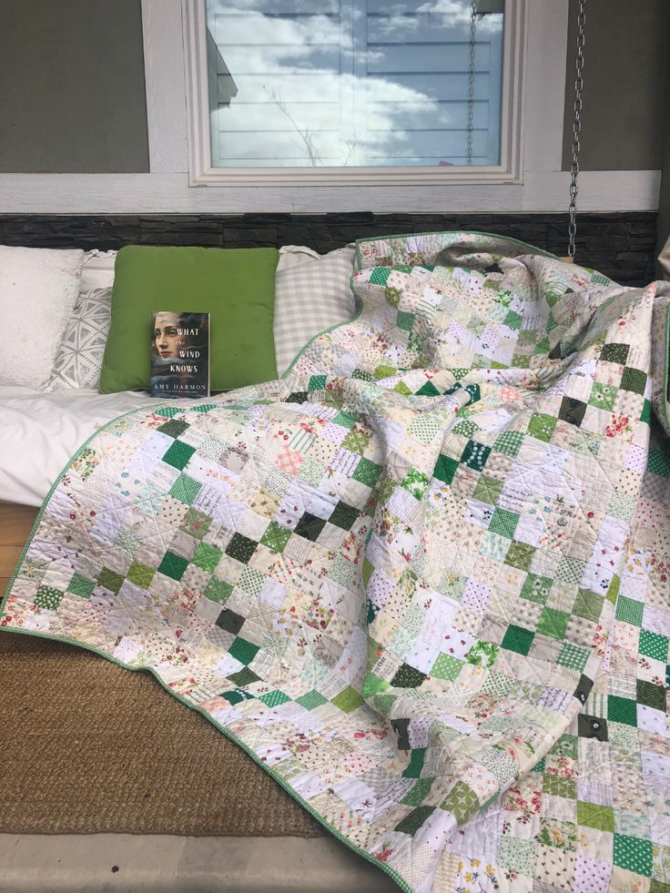 a bed with a green and white quilt on it next to a window sill