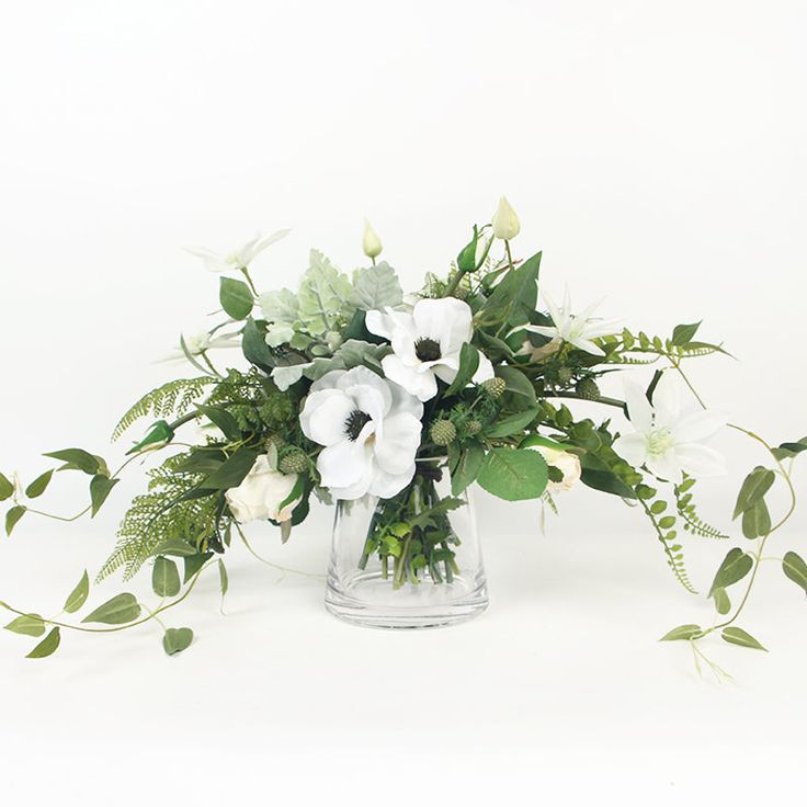 an arrangement of white flowers and greenery in a glass vase on a white background