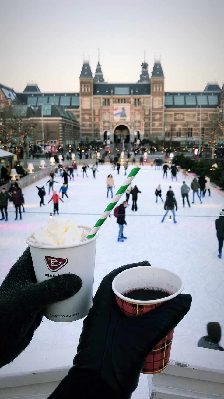 a person holding up a cup of ice cream in front of an ice skating rink