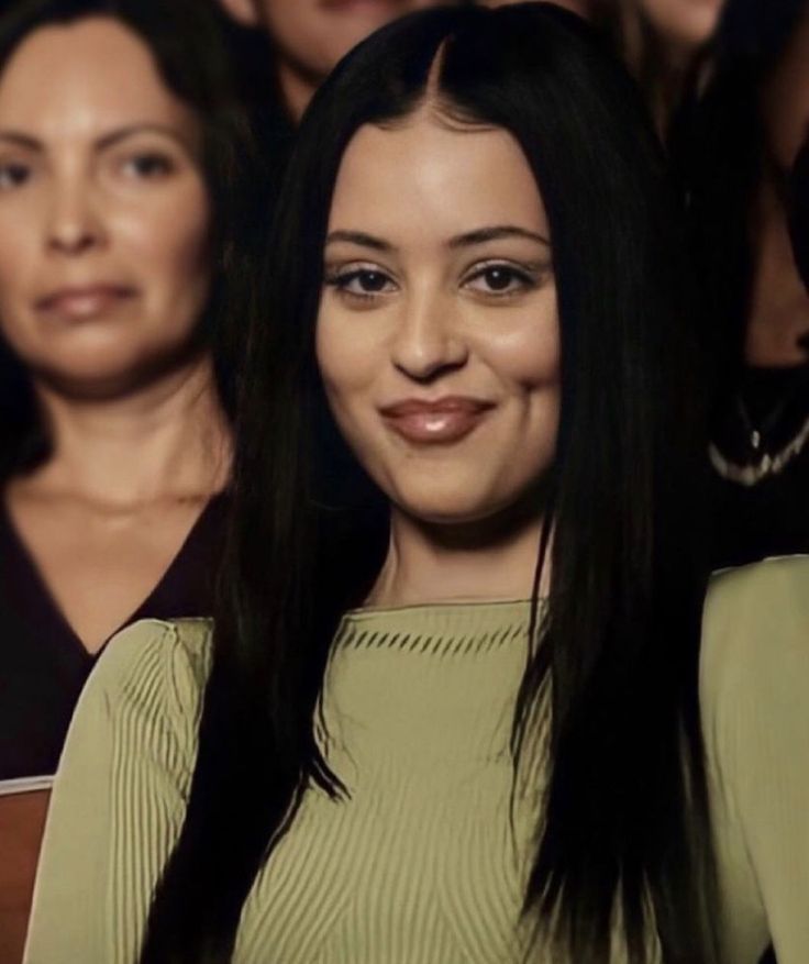 a woman with long black hair is smiling at the camera while two other women stand behind her