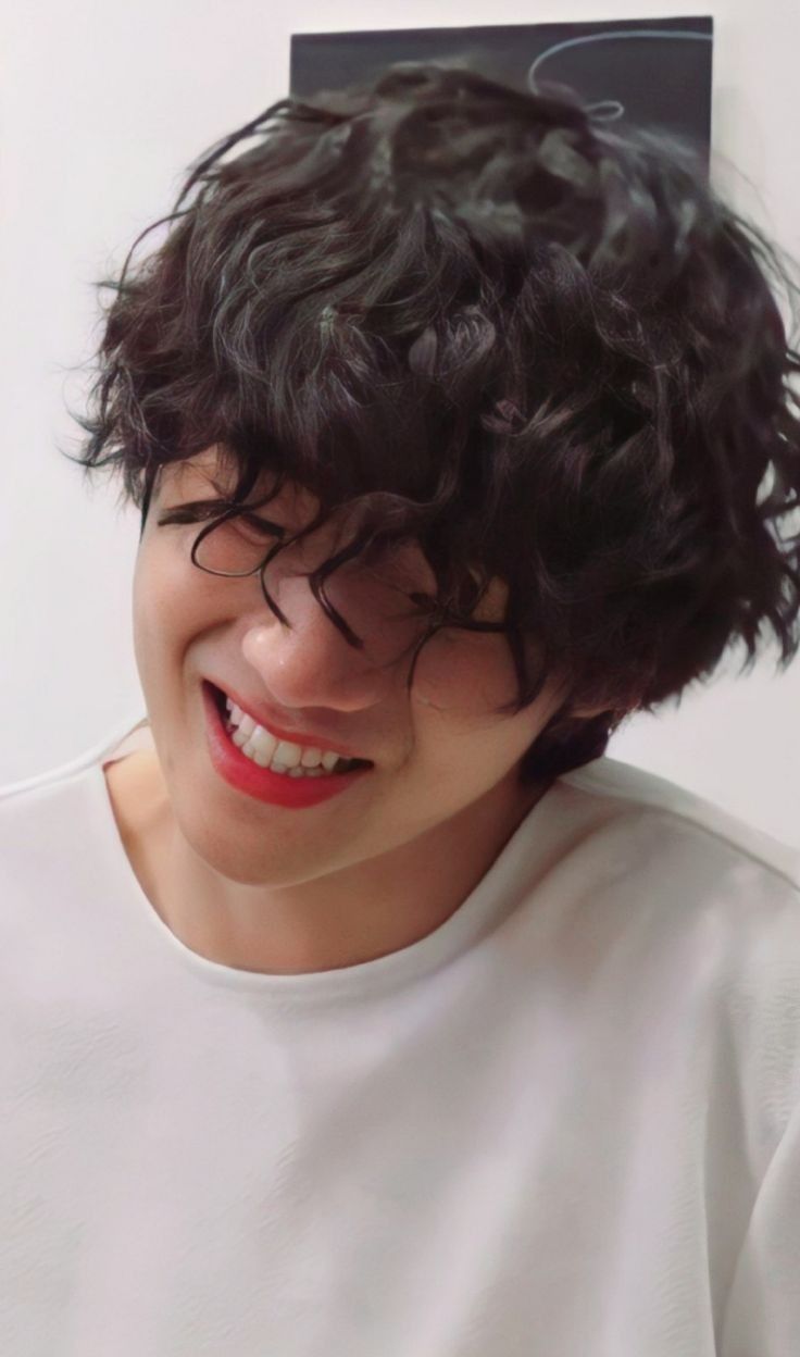 a young man with curly hair smiling and wearing a white t - shirt that has a black tag on it's head