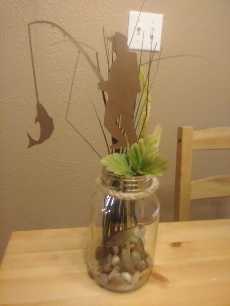 a glass jar filled with rocks and plants on top of a wooden table next to a wall