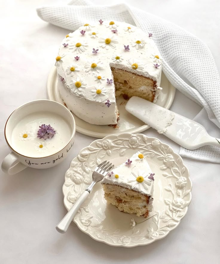 a cake with white frosting and yellow flowers on it next to a tea cup