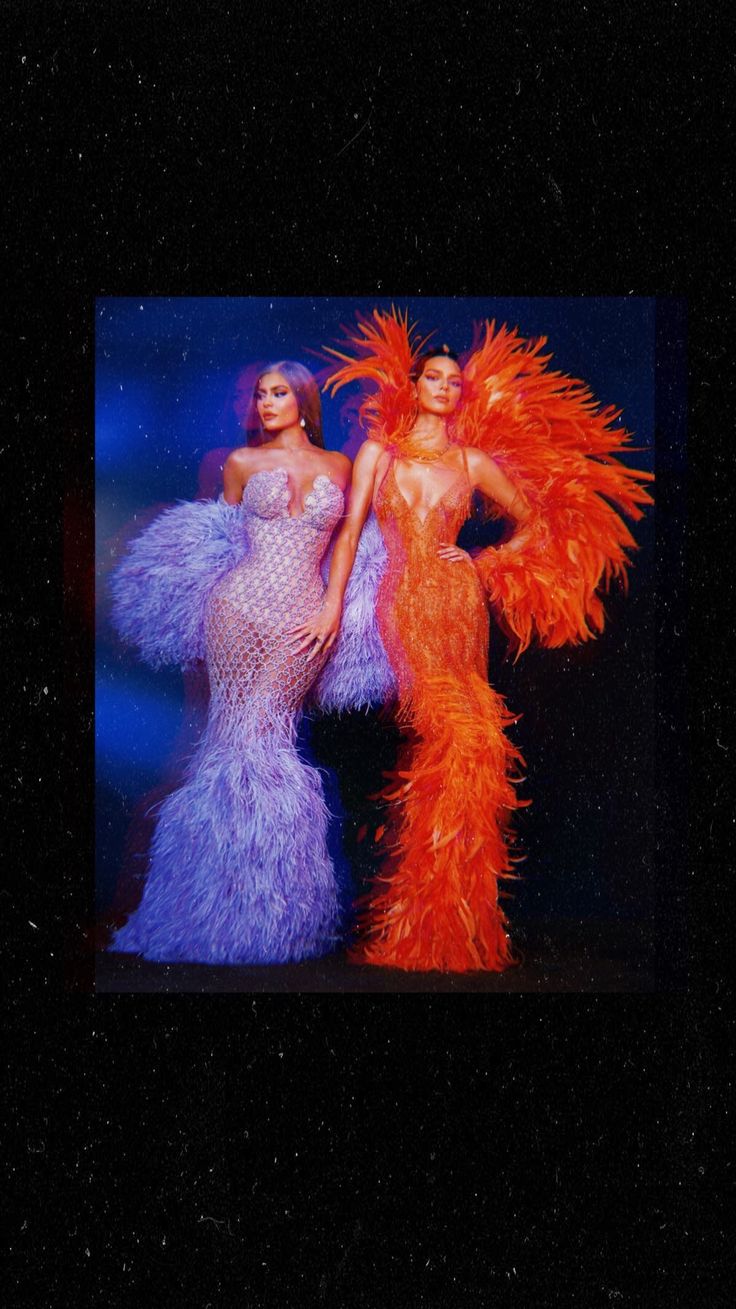 two women dressed in colorful feathered dresses standing next to each other on a stage