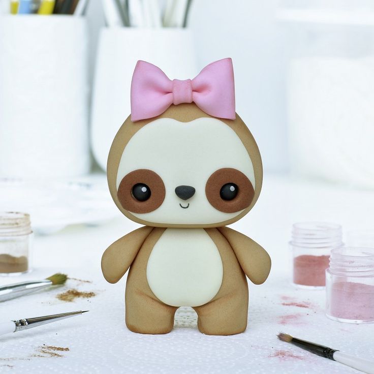 a small teddy bear with a pink bow sitting on a table next to paintbrushes