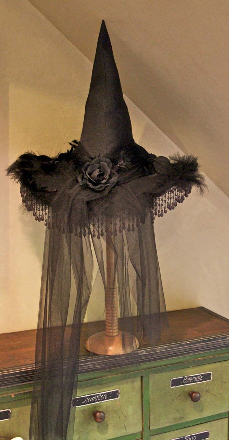 an old dresser is decorated with black fabric and feathers for halloween decorations, as well as a witch's hat on top