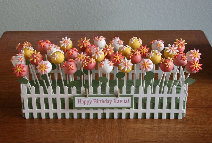 a white picket fence with pink and yellow flowers in it on a wooden table next to a sign that says happy birthday mom