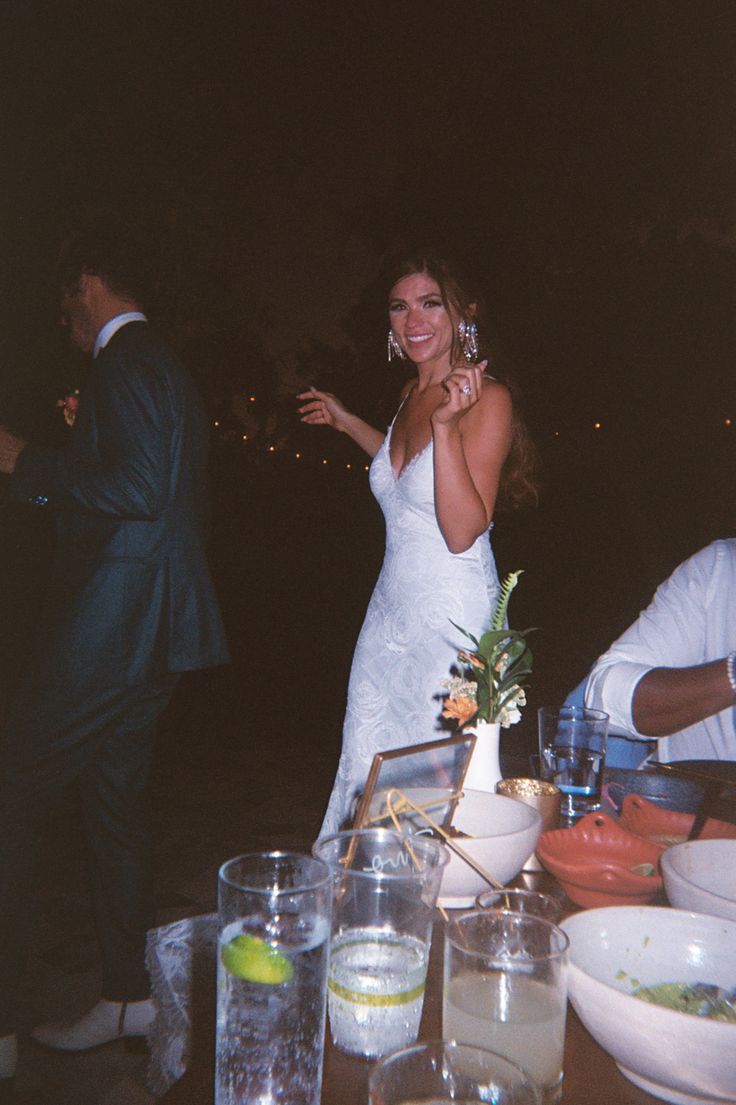 a woman in a white dress standing next to a table full of food and drinks