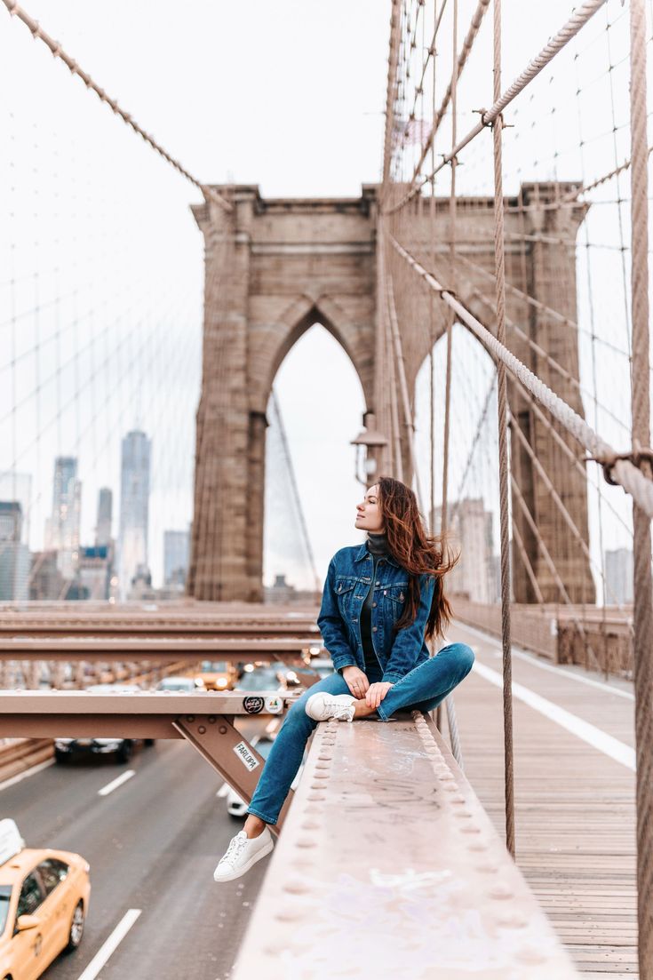 a woman sitting on the edge of a bridge looking up into the sky with cars passing by