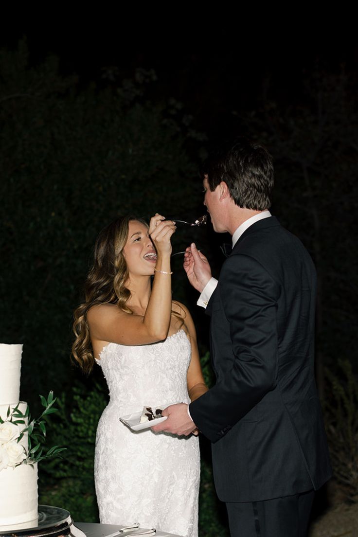 a bride and groom feeding each other cake at their wedding reception in front of the night sky