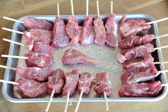 meat skewers sitting on top of a metal pan covered in salt and pepper