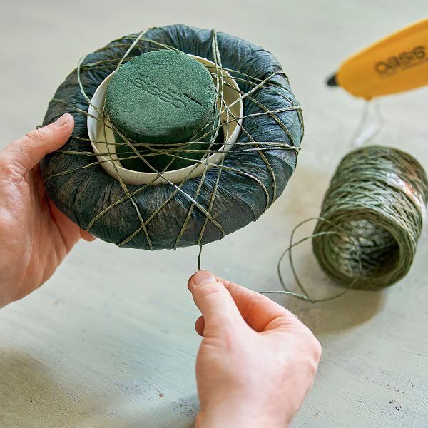 two hands are holding yarn in front of a green ball and spools of thread