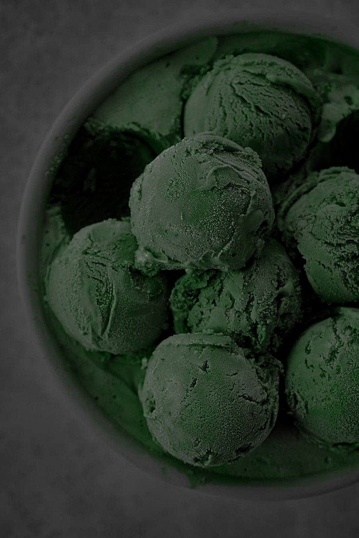 a bowl filled with green ice cream on top of a gray countertop next to a black background