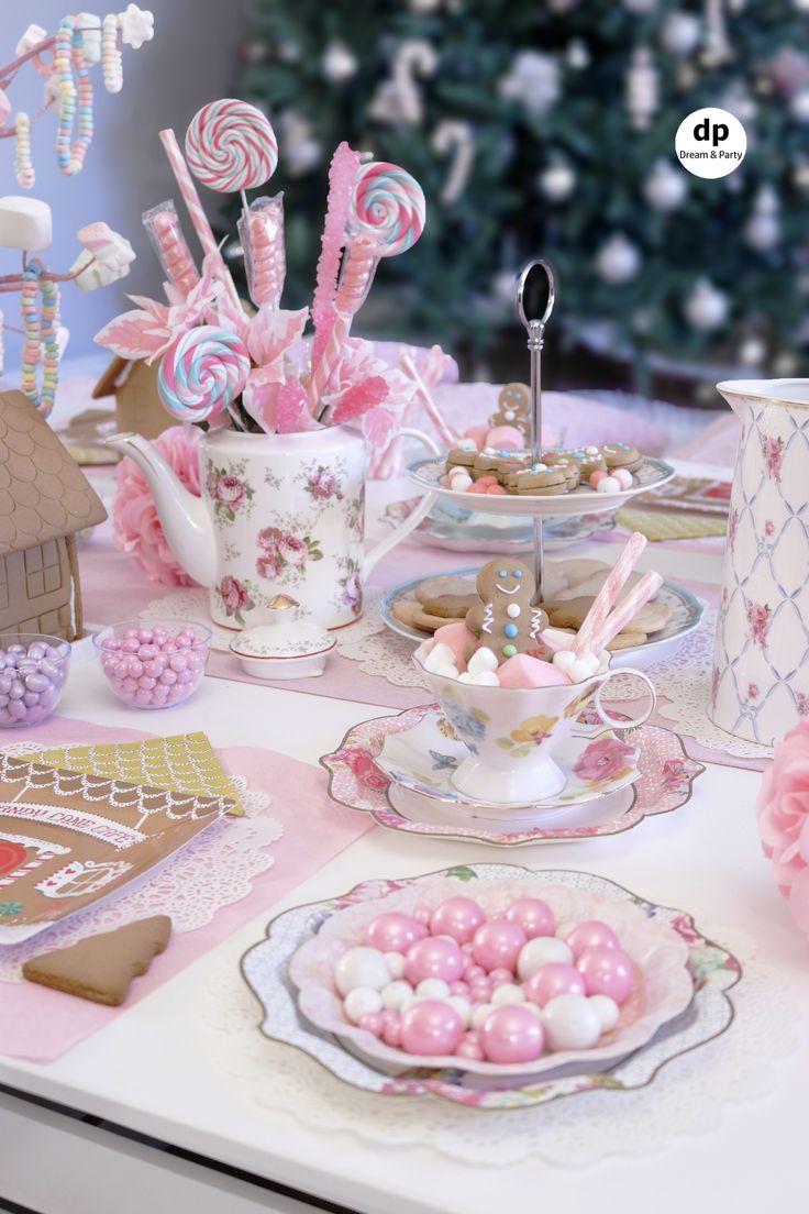 a table topped with pink and white plates filled with candies next to a christmas tree