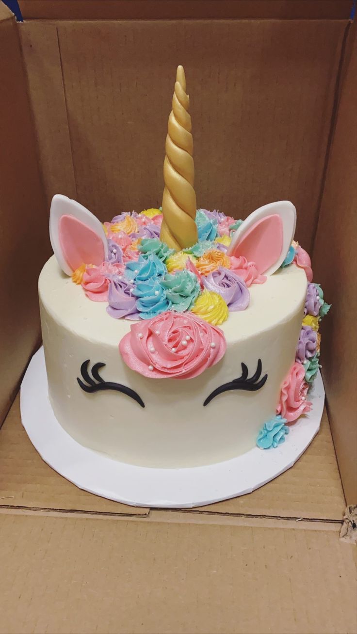 a cake in a box decorated with flowers and a unicorn's horn on top