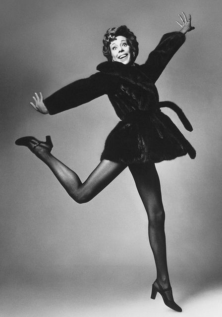 a black and white photo of a woman in a fur coat, tights and heels