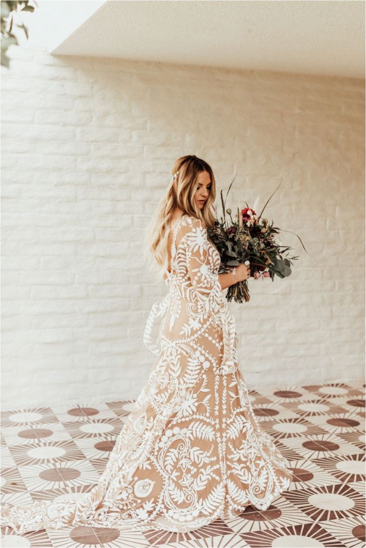 a woman in a white lace dress holding a bouquet of flowers and looking at the camera