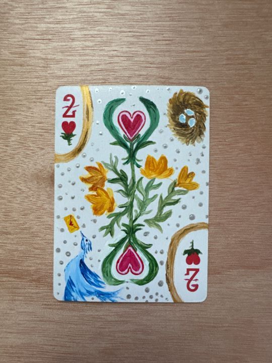 a playing card with flowers and hearts painted on the front, sitting on top of a wooden table