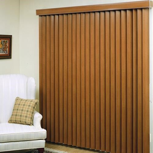 a living room with a white chair and brown vertical blinds on the sliding glass door