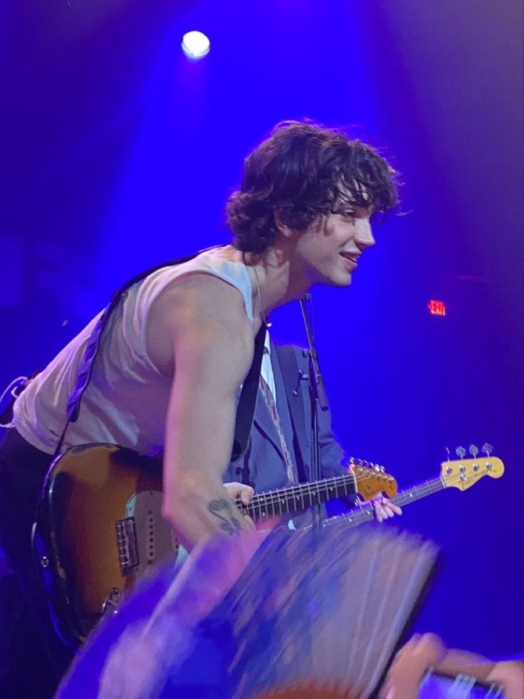 a young man playing guitar on stage with blue lights behind him and his hands in the air