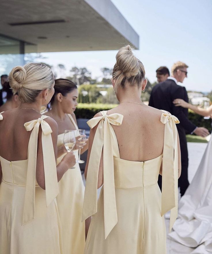 two women in yellow dresses standing next to each other with wine glasses on their laps