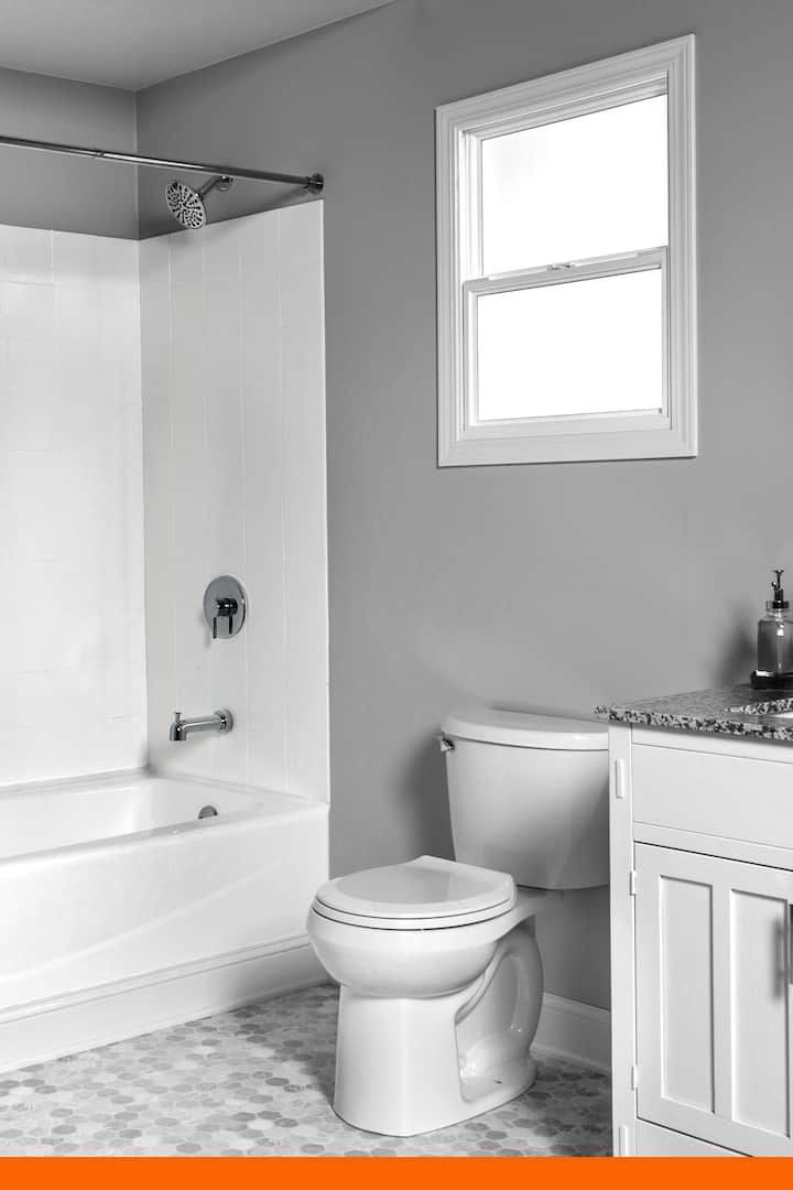 a white toilet sitting next to a bath tub in a bathroom under a window with an orange border