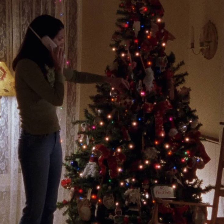 a woman standing in front of a christmas tree talking on a cell phone while holding her hand up to her ear