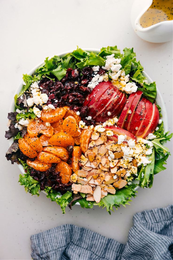 a bowl filled with salad and fruit on top of a white table next to a blue towel