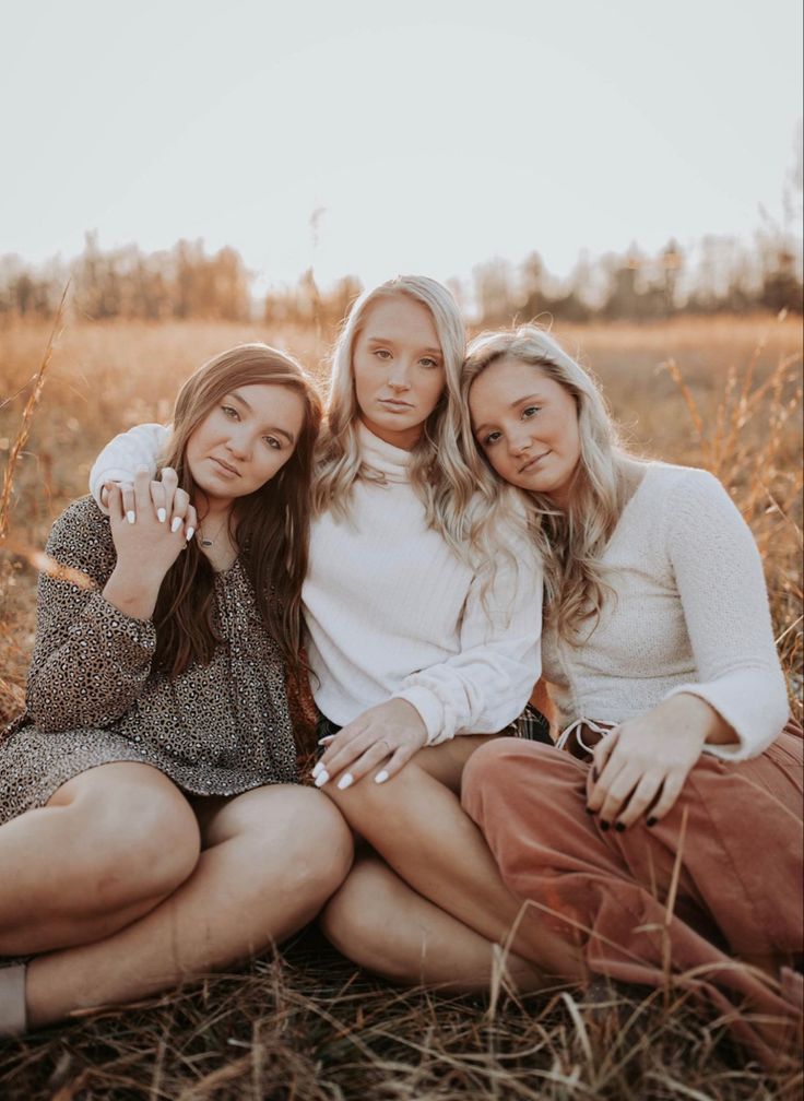 three young women sitting on the ground posing for a photo with their arms around each other