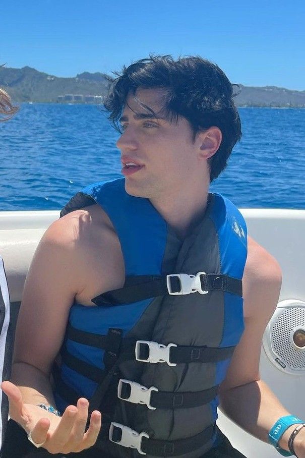 a man in a life jacket sitting on a boat with his hand out to the side