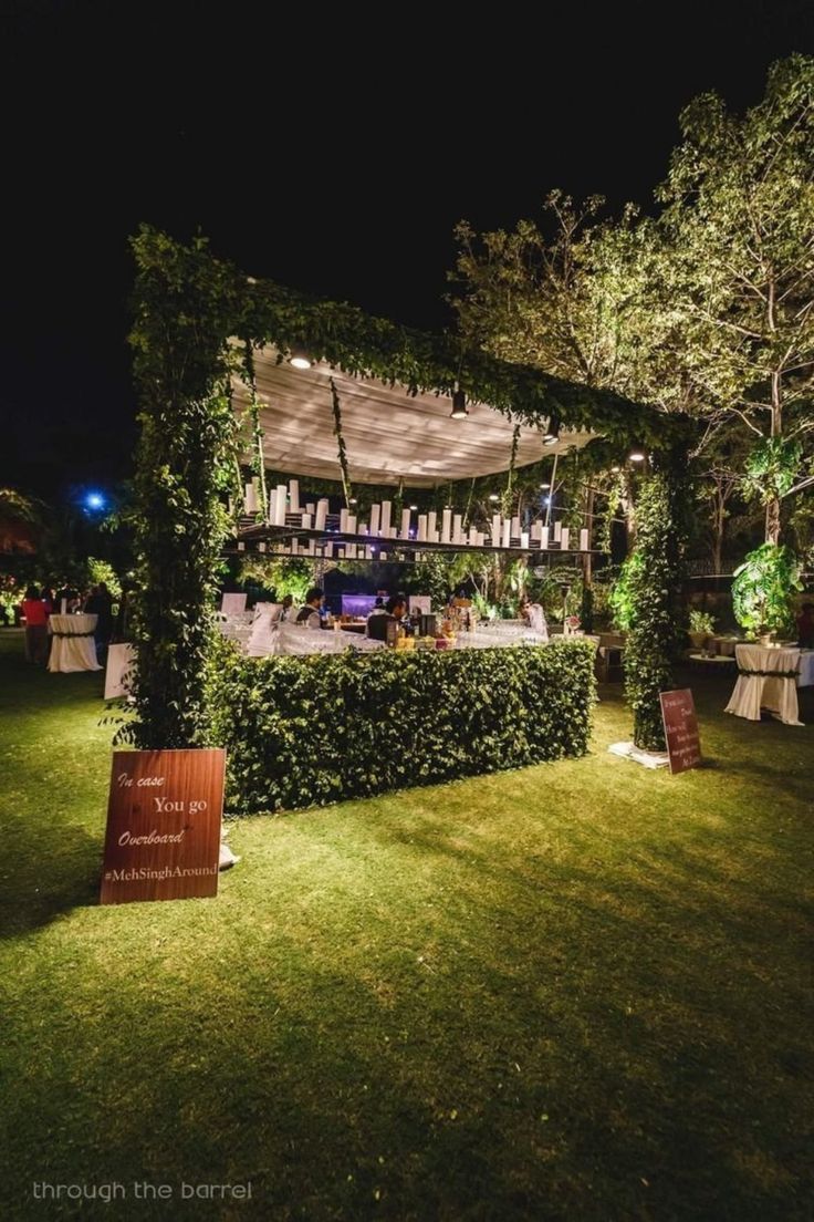 an outdoor wedding reception setup at night with greenery on the walls and tables in the middle