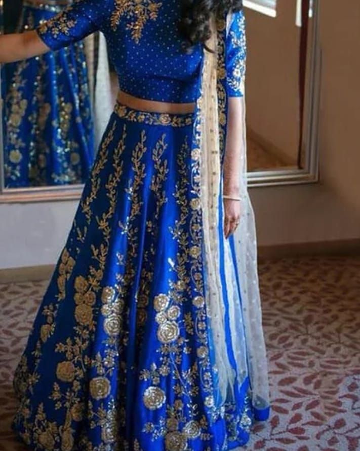 a woman in a blue and gold lehenga standing next to a mirror with her hand on her hip